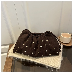 Detail of dark brown suede bucket bag with gold studs and drawstring closure