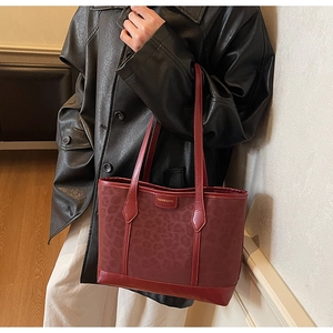 Detail of red-brown leather tote bag with leopard pattern and metal logo plate