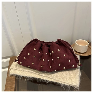 Detail of burgundy suede bucket bag with gold rivets on soft knit scarf background