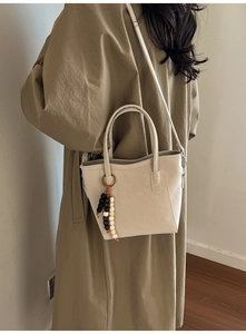 Detail of beige bucket tote bag featuring beaded charm and removable shoulder strap