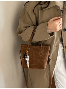 Detail of brown faux suede bucket bag with beaded charm and adjustable strap