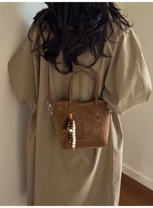 Brown frosted leather bucket bag featuring a decorative beaded pendant and shoulder strap