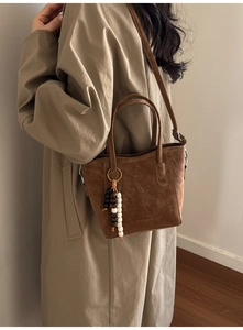 Brown suede bucket bag with wooden bead charm and long strap shown on model in studio