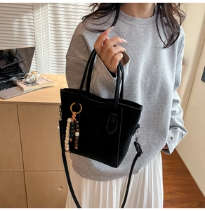 Detail of black suede tote bag with beaded charm and adjustable strap on a wooden desk