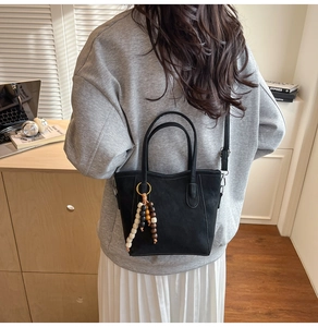 Detail of black suede tote bag featuring decorative wooden beads and tassel accent