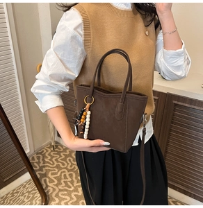 Detail of dark brown matte tote bag with rustic wooden bead charm and long shoulder strap