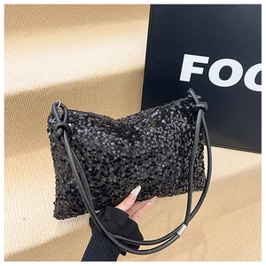 Detail of black sequin shoulder bag with leather strap and knot accent on a beige background