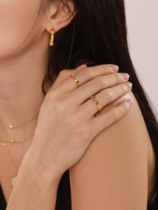 Detail of 18K gold-plated wavy ring, sparkling earrings, and layered charm necklaces on a model