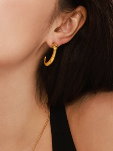 Détail de boucles d'oreilles serpent dorées avec yeux en zircon vert et écailles