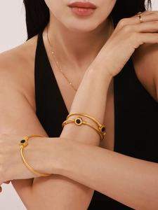 Close-up of twisted golden bangle with black shell inlay worn by a female model