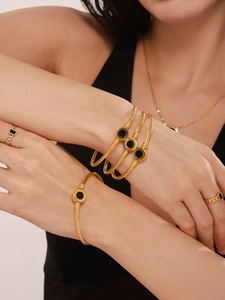 Detailed close-up of gold layered bracelets with black shell inlays and textured rings
