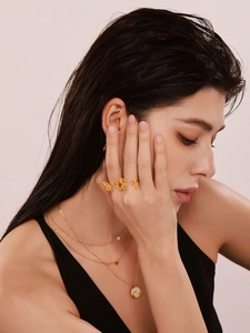 Detail of model wearing a 18K gold butterfly ring and layered pearl pendant necklaces