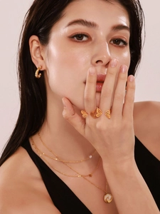 Close-up of layered 18k gold butterfly rings and pearl star necklaces on model