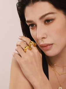 Irregular gold wave ring worn on finger with layered necklaces in warm lighting