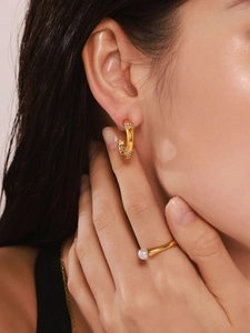 Close-up of elegant gold C-shaped zircon earrings and round pearl ring on a model