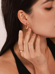 Close-up of elegant gold C-shape crystal earrings and pearl ring on model's hand