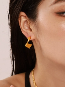 Close-up of golden irregular pleated C-shaped earrings worn on an elegant model