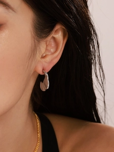 Close-up of a silver irregular fluid metal C-shaped earring on a woman's ear