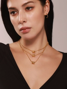 Detail van de drielaagse gouden cilinderketting en de gedraaide goudkleurige oorbellen