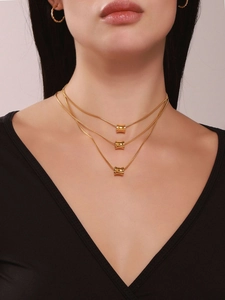 Detailopname van drielaagse gouden slangenkettingen met minimalistische cilinderhangers