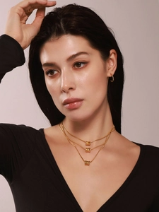 Detail van een gelaagde 18K vergulde ketting met cilindervormige hangers gedragen door model