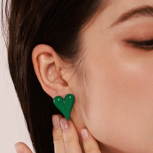 Emerald green enamel heart stud earrings in stainless steel on female model ear