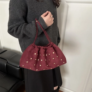 Retro burgundy suede bucket bag with gold rivets and drawstring handle held by a model