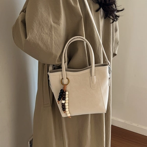 Beige bucket bag with beaded charm and shoulder strap on a model in a khaki coat