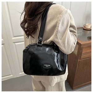 Détail du sac Boston en cuir verni noir avec anneaux argentés et étiquette mode
