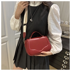 Detail of dark red crossbody bag with wide fabric strap and golden metal hardware
