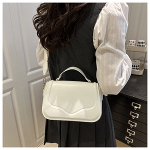 Close-up of white leather crossbody bag with wave embossed flap and wide shoulder strap
