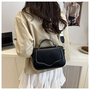Detail of a black leather crossbody bag featuring a wide white canvas shoulder strap