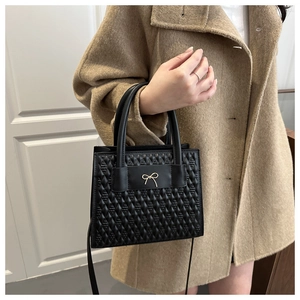 Detail of black textured PU leather handbag with golden bow decoration and top handle