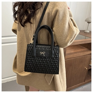 Detail of black textured PU leather handbag with gold bow and quilted diamond pattern