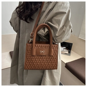 Detail view of brown quilted bag with gold bow clasp and adjustable shoulder strap