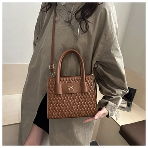 Detail of caramel brown quilted handbag featuring a golden bow accent and leather strap