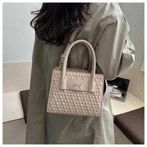 Detail of cream quilted handbag with metal bow and adjustable shoulder strap