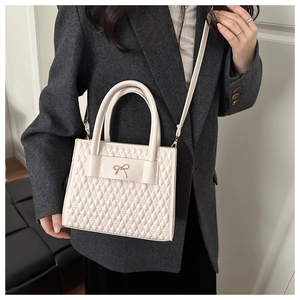 Detail of cream quilted crossbody bag with gold bow clasp worn over a grey blazer