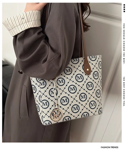 Macro view of patterned tote bag showing blue M print and gold letter charm detail