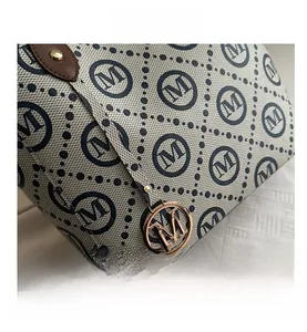 Close-up of cream tote bag featuring navy M-monogram print and golden logo pendant