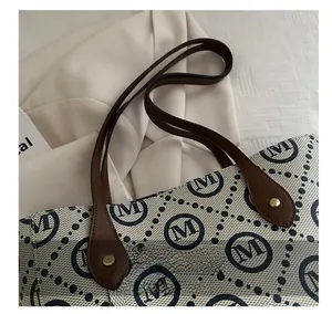 Detail of canvas tote bag with monogram print and leather handle fixed by rivets