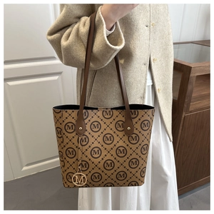 Detail of brown monogram tote bag featuring leather handles and gold M metal pendant charm