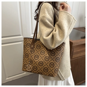 Detail view of brown tote bag with repeating M-logo pattern and gold metal pendant