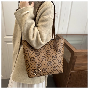 Brown monogram tote bag with gold M pendant worn on shoulder for stylish daily commute