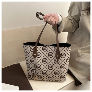 Detail of cream tote bag featuring monogram print and golden M letter charm pendant