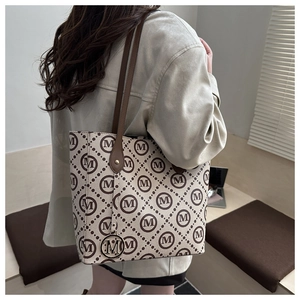Detail view of tote bag with M-pattern print, gold pendant and slim brown shoulder strap
