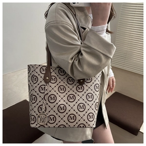 Detailed close-up of a large tote bag with M-pattern print and a round metal M-logo charm
