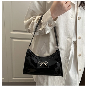Detailed view of the black patent leather shoulder bag with a gold metal bow accessory