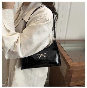 Detail of black glossy PU leather hobo bag with a golden bow buckle on the strap