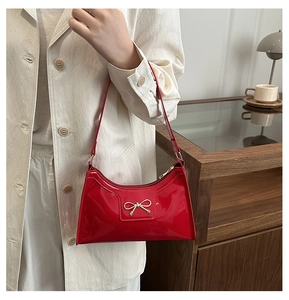 Detail of red patent leather shoulder bag with a gold metal bow and smooth mirror finish
